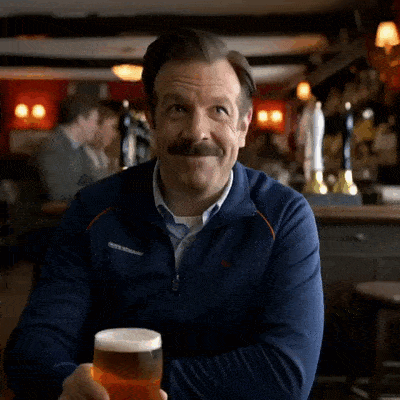 Ted Lasso sourit et lève sa chope pour trinquer.
