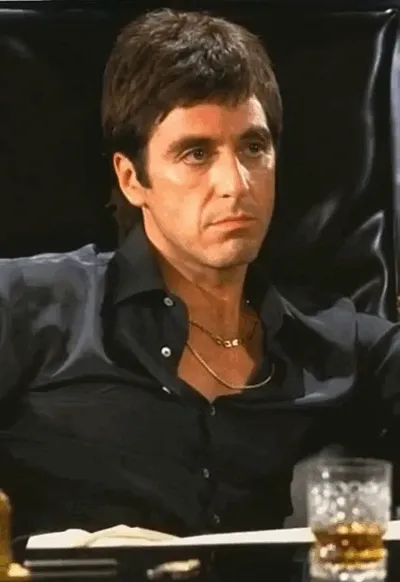 Al Pacino, assis à une table, passe d’un air sérieux à un rire moqueur.