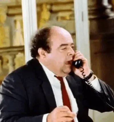 Un homme en costume parle au téléphone en faisant un geste de la main.