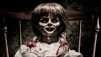 A creepy doll with red braids sits on a wooden chair in the shadows.