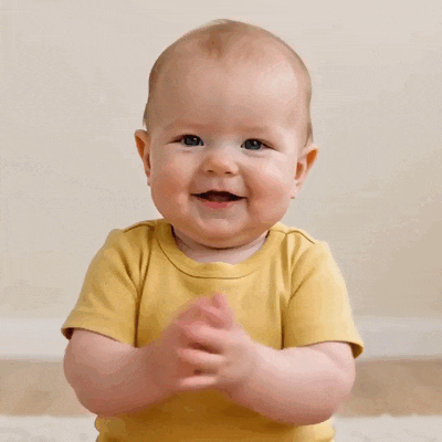 Un bébé souriant en haut jaune applaudit.
