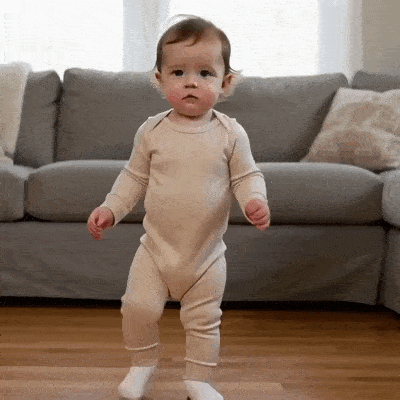 Un bébé debout devant un canapé regarde autour de lui avec méfiance.