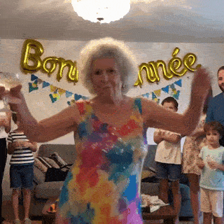 Une mamie en robe colorée danse en famille sous des ballons Bonne année.