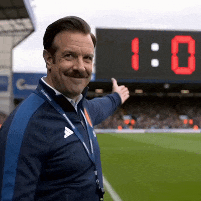 Ted Lasso montre le score et célèbre la victoire de son équipe.